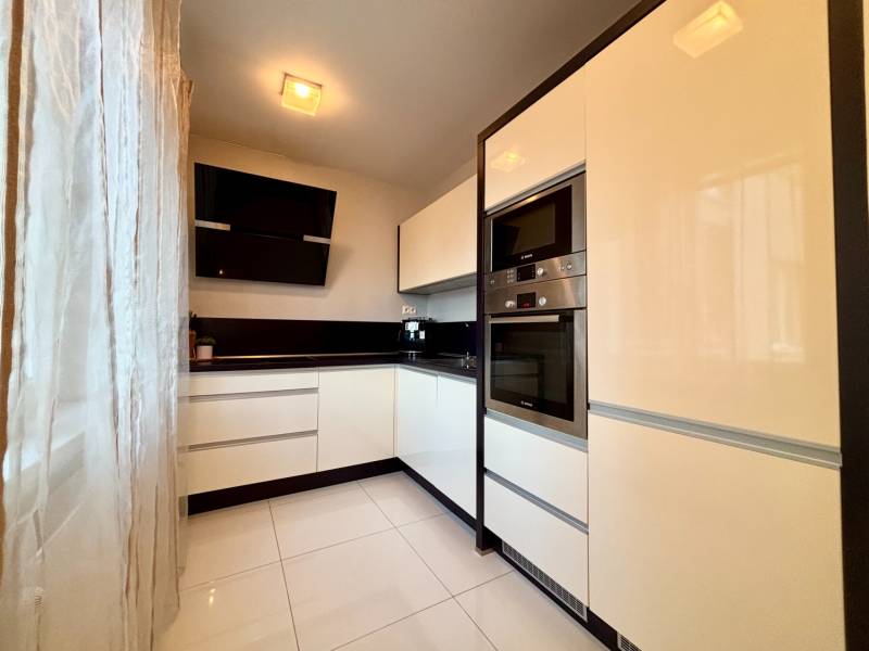 White kitchen with black accents and appliances in a 2-room apartment.