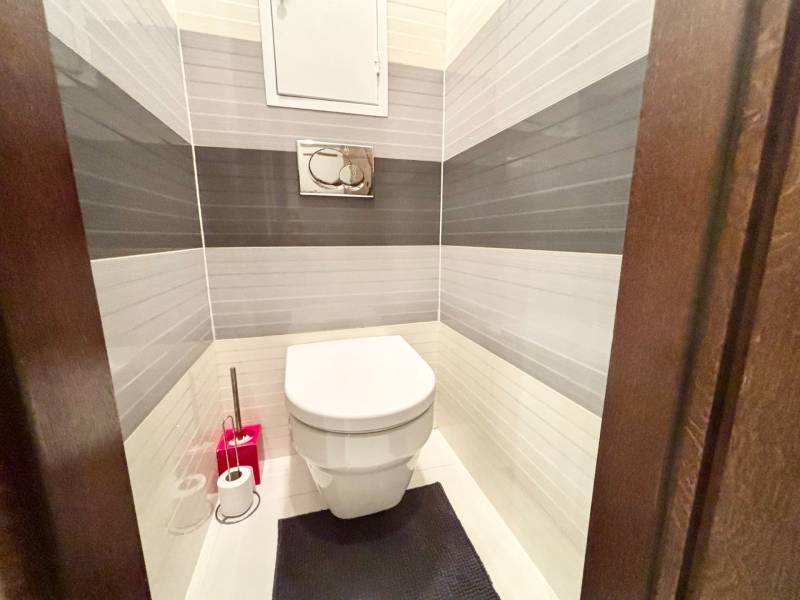 A toilet in a 2-room apartment with white and gray tiles on the walls.