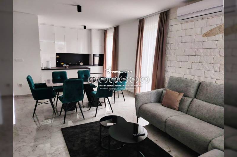 Living room with kitchen in a family house; marble floor, white cabinets, green chairs.