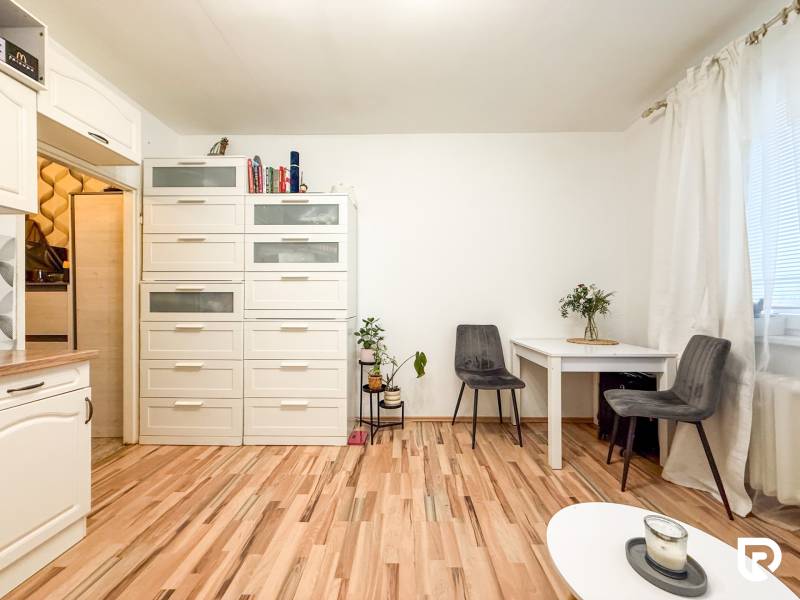 Studio apartment with wood-patterned flooring, a white table and chairs, and cabinets with storage space.