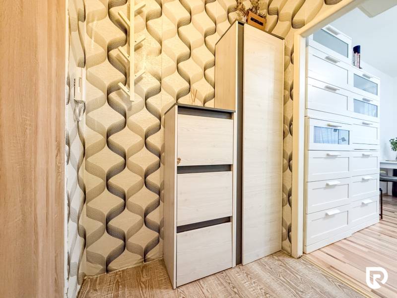 Wallpaper with a geometric pattern, white cabinets, and a wooden decor floor in a studio apartment.