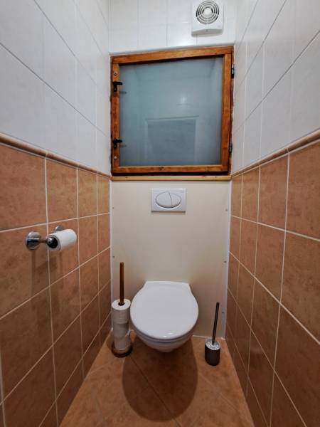 A toilet in a 3-room apartment with ceramic tiles and a toilet window.