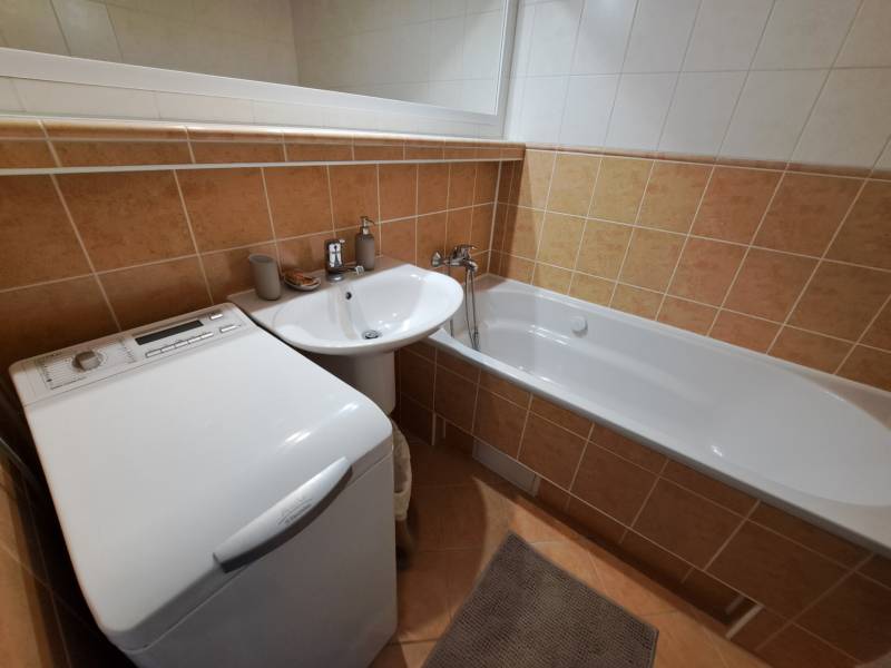 A bathroom in a 3-room apartment with a bathtub, sink, and washing machine, tiled with orange tiles.