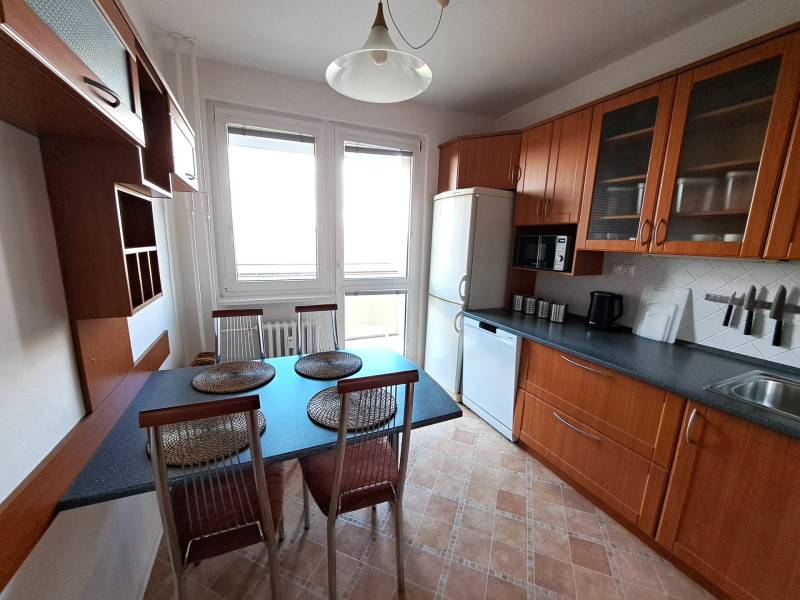 A kitchen in a 3-room apartment with a dining table, appliances, and cabinets with a wooden decor.