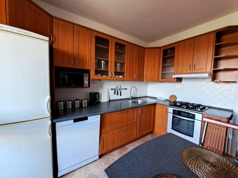 A kitchen in a 3-room apartment with corner cabinets and appliances, floor with wooden decor.