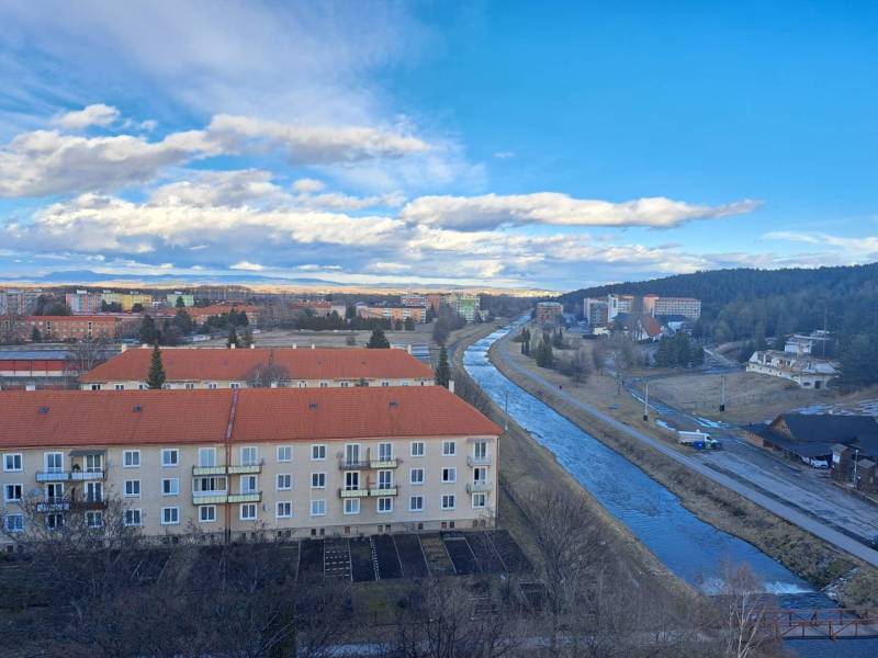 View of the town of Svit with a river, apartment buildings, and a forest in the distance.