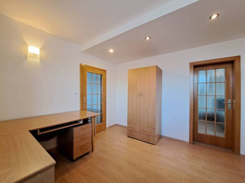A room in a 4-room apartment with a wooden decor floor, a table, and a wardrobe.