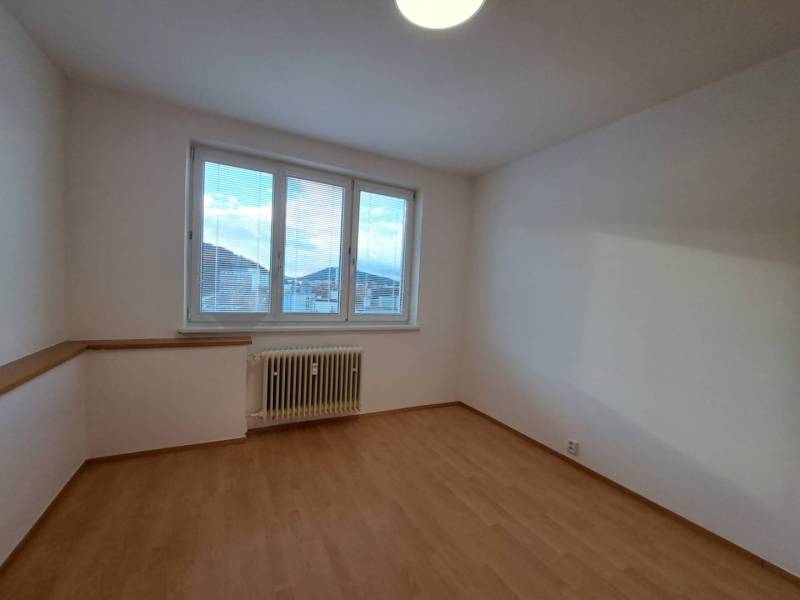 A room in a 4-room apartment with a wood-patterned floor and a large window.