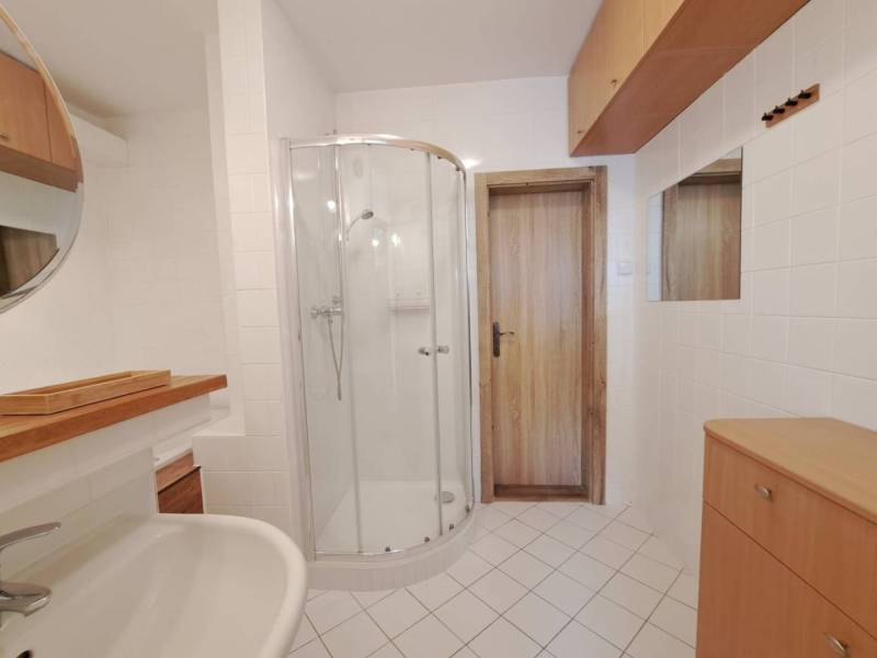 A bathroom in a 4-room apartment with white tiles, a shower corner, and wooden elements.
