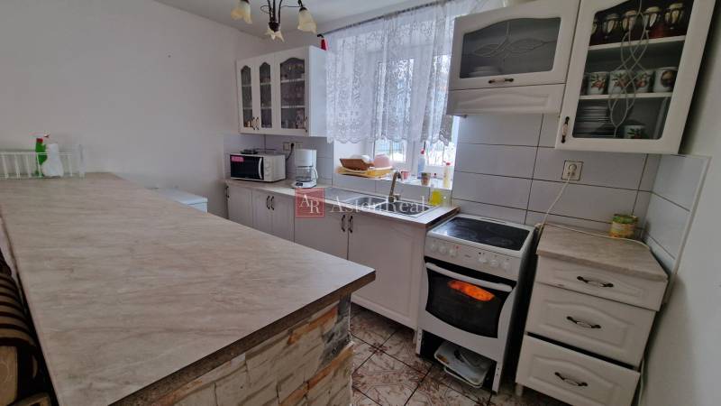 A kitchen in a family house with white cabinets, appliances, and a curtain on the window.