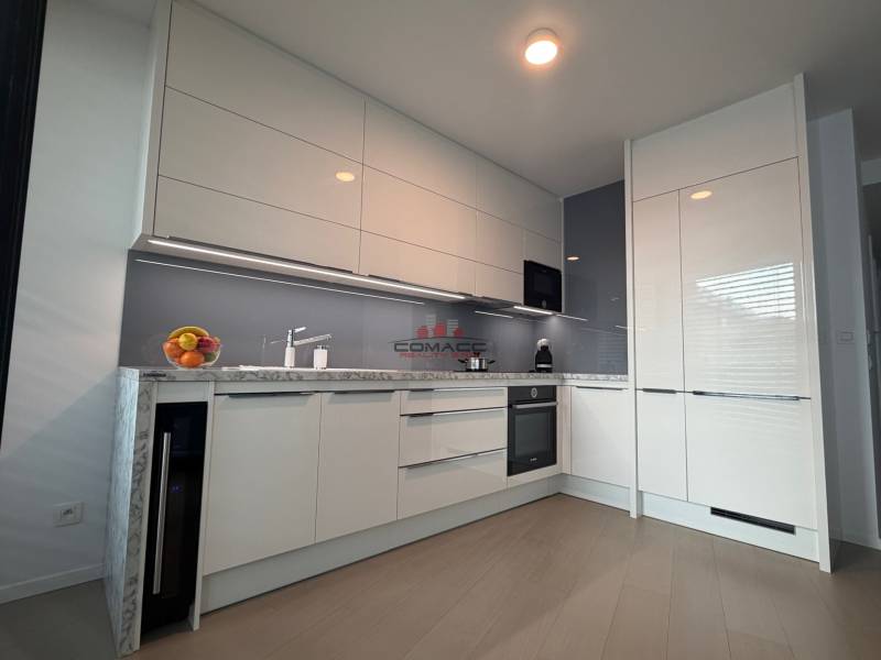 Modern kitchen in a 2-room apartment with wood-patterned flooring and white cabinets.