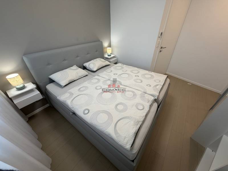 Bedroom with a double bed and a wood-patterned floor in a two-room apartment.