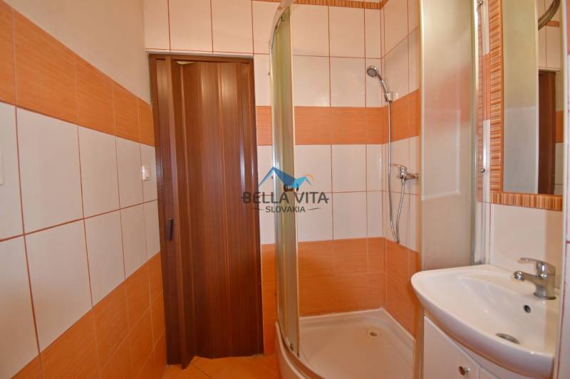 A bathroom in a studio apartment with tiles and a shower corner, in orange and white design.
