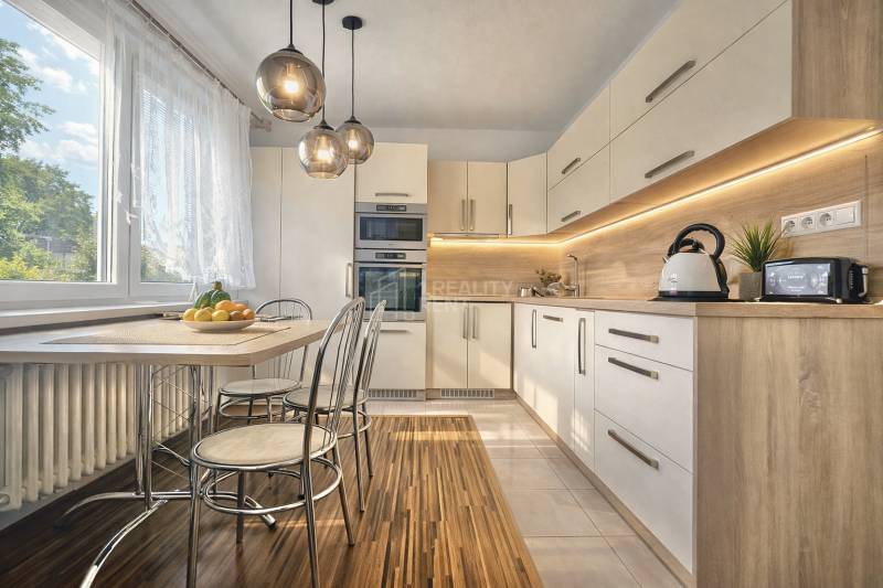 Kitchen in a 4-room apartment with a large window, wooden decor flooring, and a dining table.