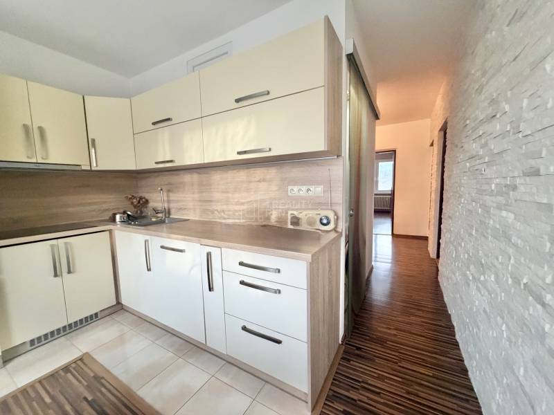 A kitchen in a 4-room apartment with a wooden decor floor and light cabinets.