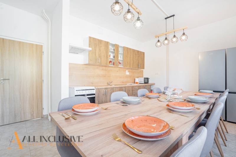 A kitchen with a large table, chairs, lights, and a kitchen unit with a wooden decor.