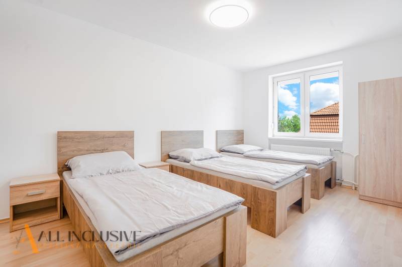 Three beds in a room with a wooden floor and a large window.