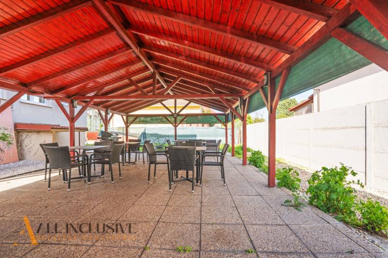 A gazebo in Dunajská Streda with a wooden roof, chairs, and tables on a concrete surface.
