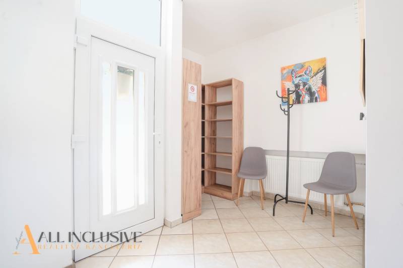 Interior of a building with entrance doors, tiles, a shelf, two chairs, and a coat rack.