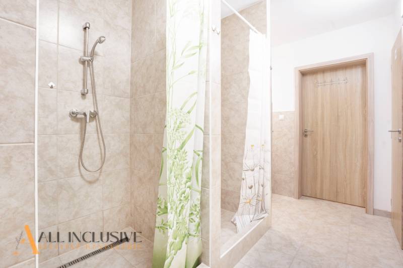 A bathroom with ceramic tiles, a shower enclosure, and wooden doors.
