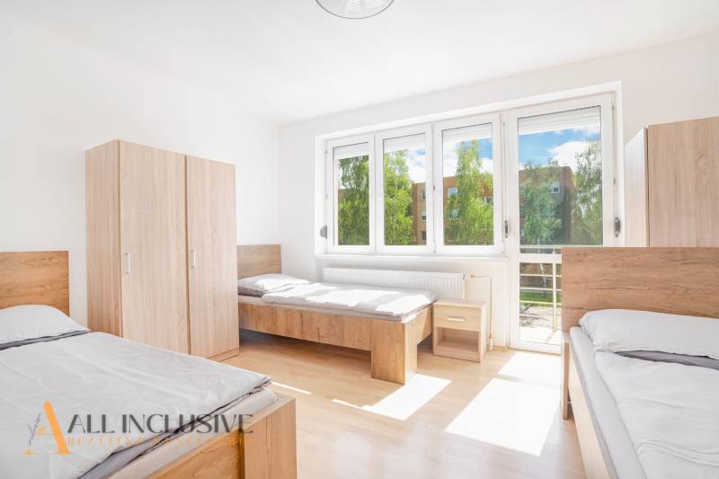 A bright room with three beds, white walls, wardrobes, and large windows.