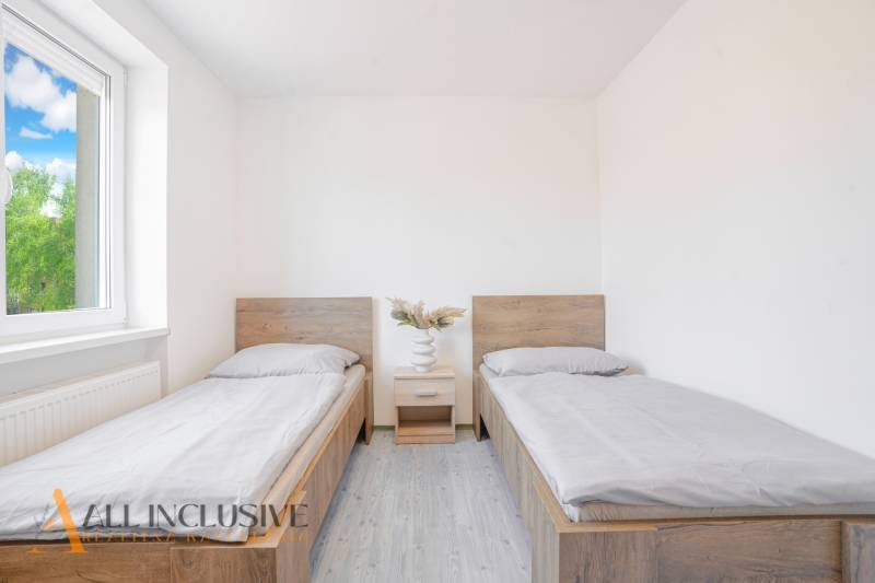 A room with two beds, a nightstand, and a floor with a wooden decor.