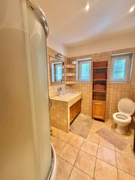 A bathroom in a family house with ceramic tiles, a shower enclosure, and storage space.