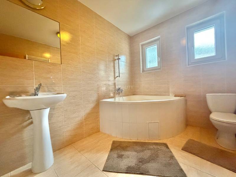 A bathroom in a family house with a bathtub, sink, and toilet, tiled with light tiles.