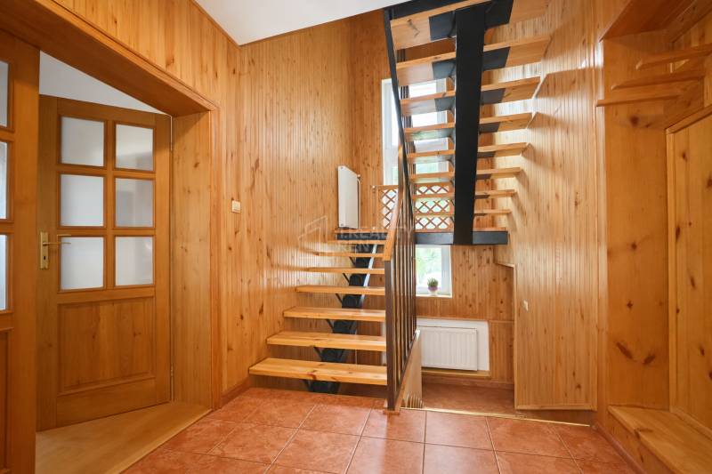 A hallway in a family house with wooden paneling, a staircase, and ceramic tiles.