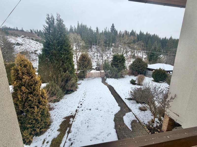 A snowy garden of a family house in Čadca on Čadečka street with coniferous trees and a lawn.