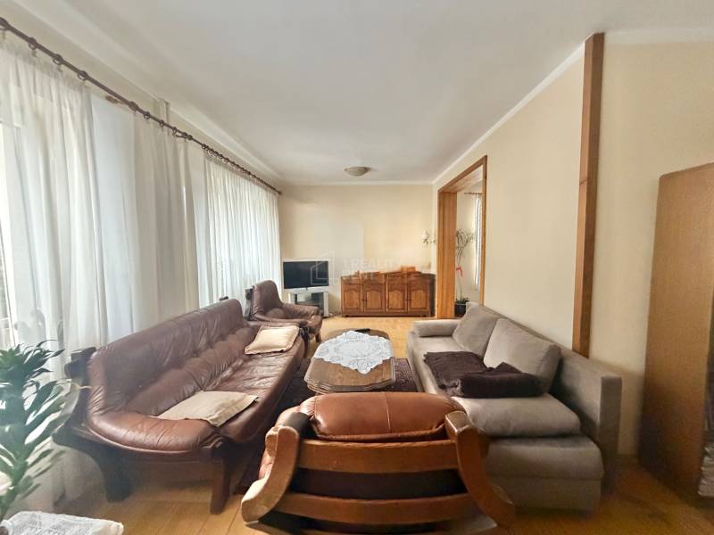 Living room in a family house with a wooden decor floor, a sofa, and curtains.