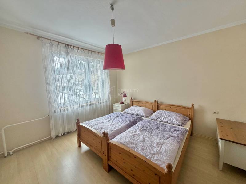 Bedroom with a double bed and a chandelier in a family house with a wood-patterned floor.