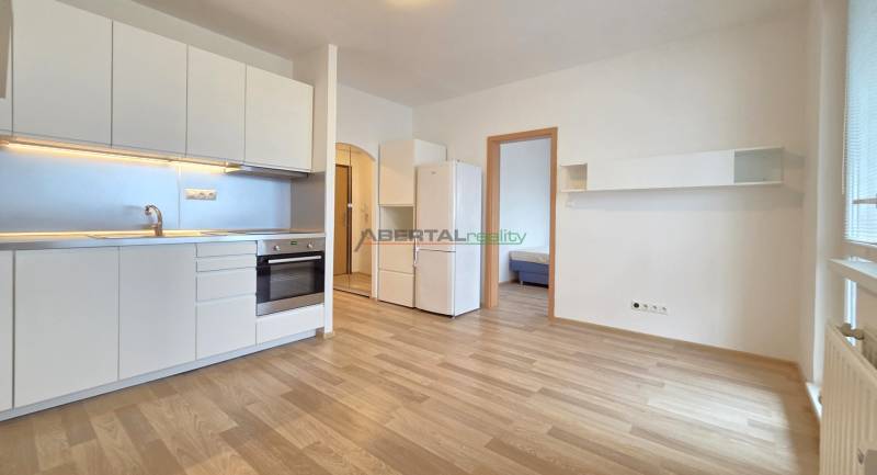 A kitchen in a studio apartment with white cabinets and a wooden decor floor.