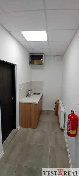 A narrow office kitchenette with a sink, fire alarm, and white walls.