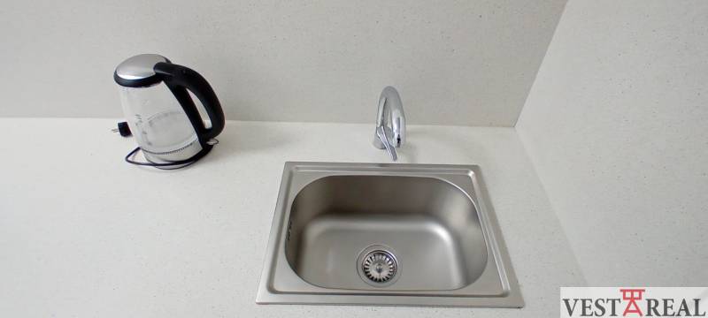 A kitchen sink with a kettle on a white countertop in an office.
