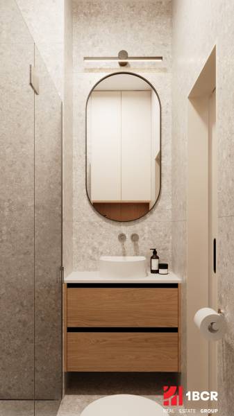 A bathroom in a 4-room apartment with an oval mirror and wooden cabinets.