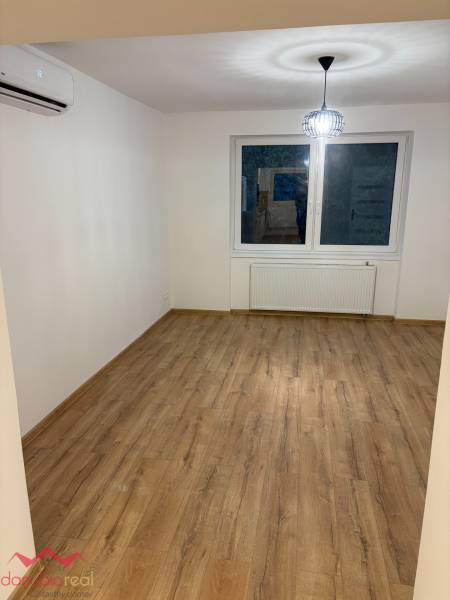 A room in a 3-room apartment with a window, a light fixture, and a floor with a wooden decor.
