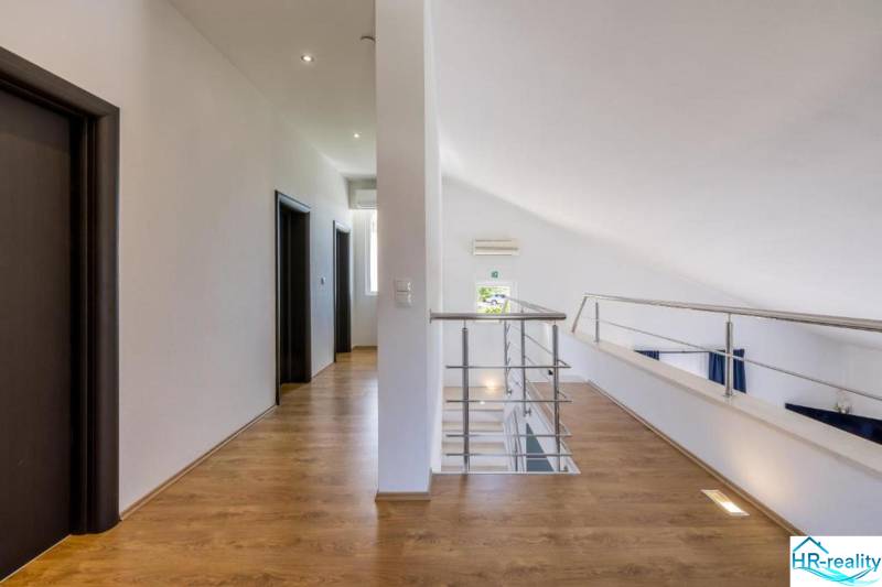 Interior of a villa with white walls, a floor with a wood decor, and a railing.