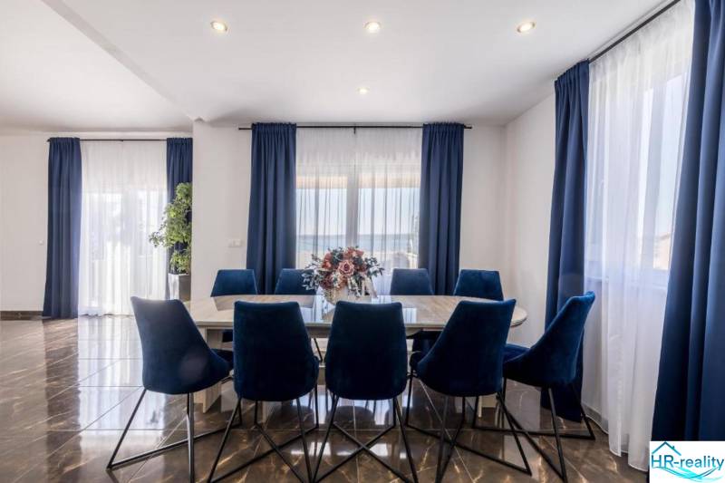 Dining room in the villa with dark curtains, wood-patterned flooring, and blue chairs.