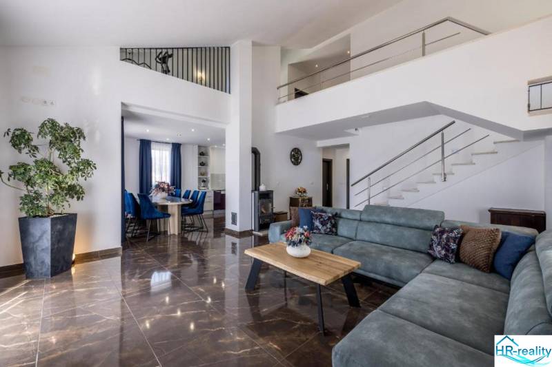 Living room of a villa with a comfortable sofa, dining area, and staircase, floor with wooden decor.