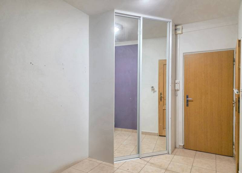 Entrance hall in a 2-room apartment with tiles and a mirror on the wardrobe.