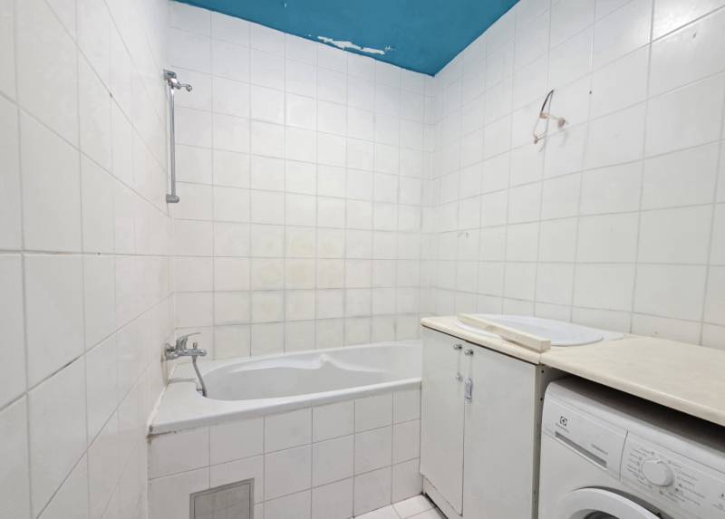 Bathroom in a 2-room apartment with a bathtub, white tiles, and a washing machine.