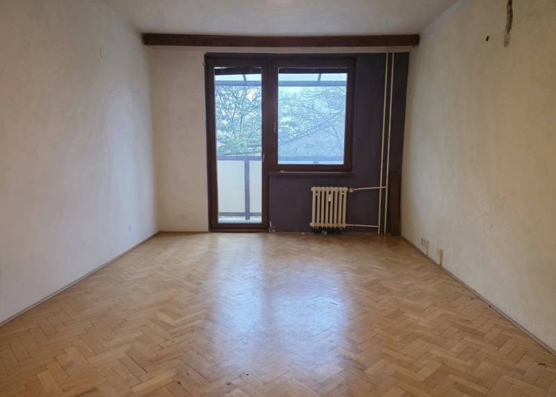 A room with a wooden floor decor, a large window, and a radiator in a 2-room apartment.