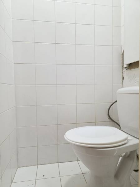 A toilet in a 2-room apartment with white tiles and flooring.
