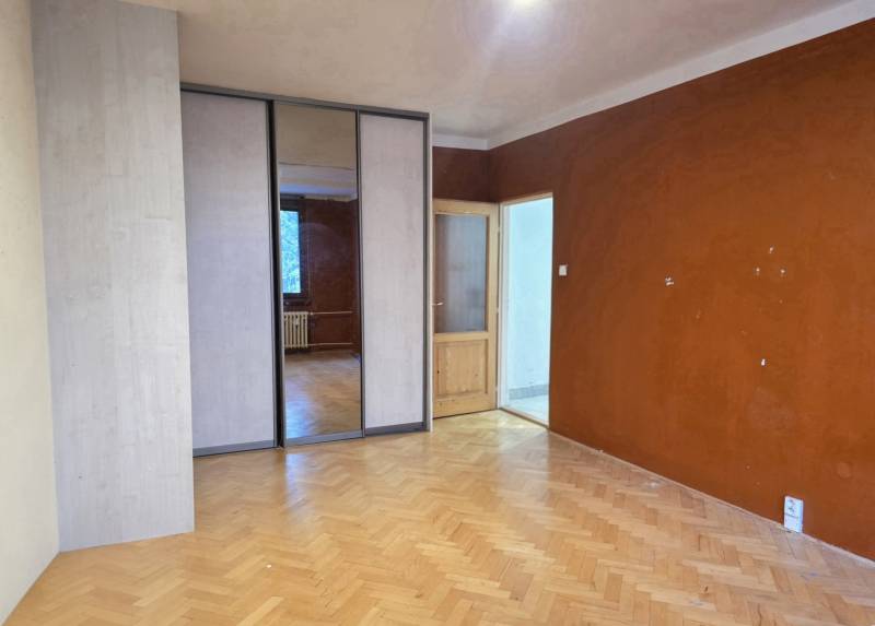 A room in a 2-room apartment with a wood-decor floor and wardrobes with sliding doors.