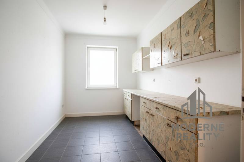 A kitchen in a family house with older cabinets and tiles on the floor.