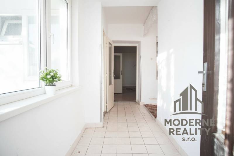 A hallway in a family house with white walls and tiles, a flower on the windowsill.