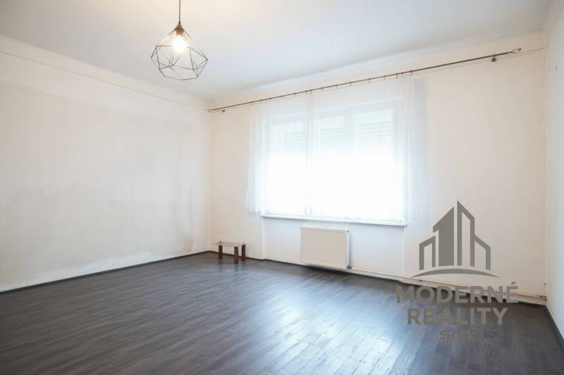 A room in a family house with a wood-patterned floor and a large window.