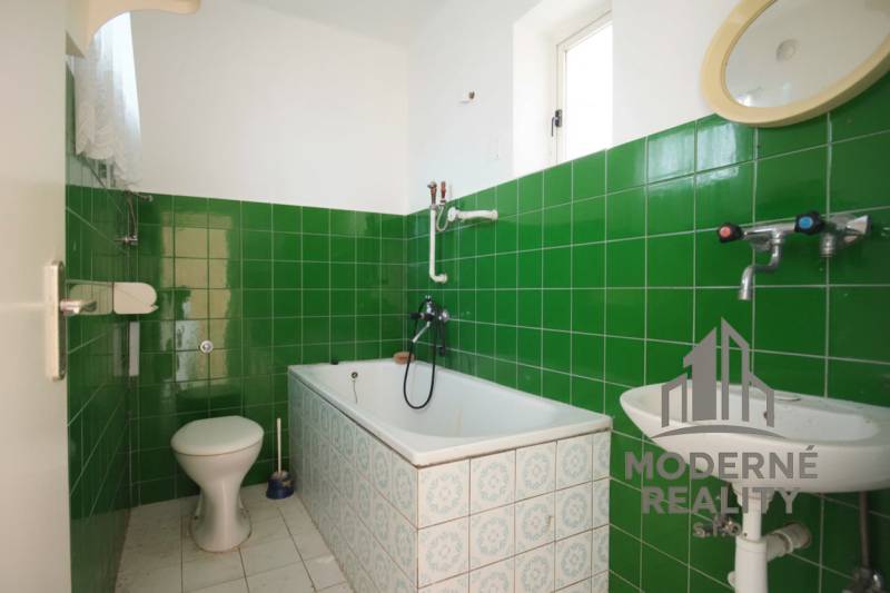 A bathroom in a family house with green tiles and a classic bathtub.