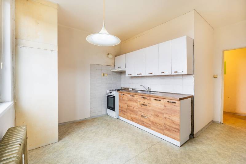 A kitchen of a two-room apartment with white cabinets and a wooden decor floor.